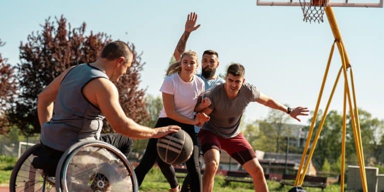Persone che giocano a basket all’aperto, tra cui un atleta in sedia a rotelle