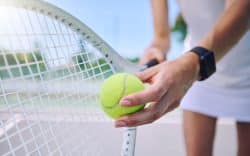 Mano che tiene una pallina da tennis vicino alla racchetta