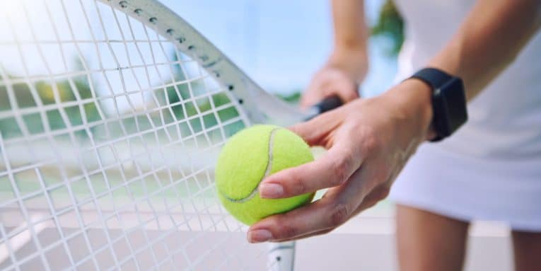 Mano che tiene una pallina da tennis vicino alla racchetta