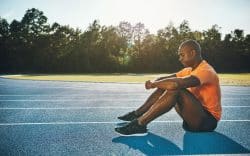 Atleta seduto su pista da corsa con le braccia appoggiate alle ginocchia
