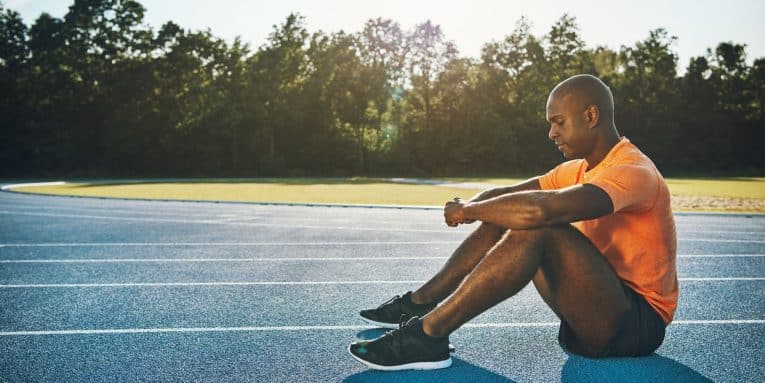Atleta seduto su pista da corsa con le braccia appoggiate alle ginocchia