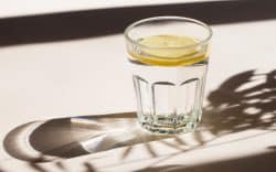 Bicchiere di vetro con acqua e limone su tavolo con luce naturale
