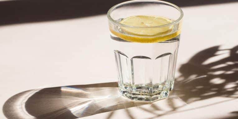 Bicchiere di vetro con acqua e limone su tavolo con luce naturale
