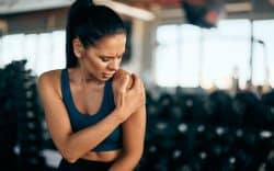 Donna in palestra con mano sulla spalla e espressione sofferente