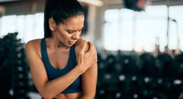 Donna in palestra con mano sulla spalla e espressione sofferente