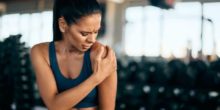 Donna in palestra con mano sulla spalla e espressione sofferente