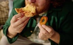 Uomo che mangia una fetta di pizza e tiene un anello di cipolla