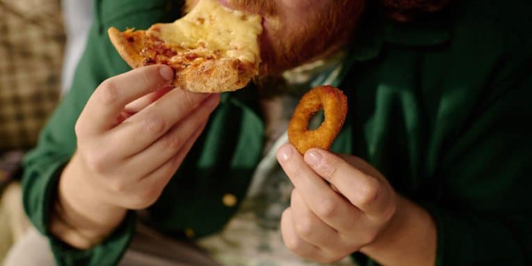 Uomo che mangia una fetta di pizza e tiene un anello di cipolla