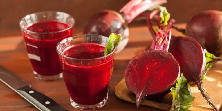 Succo di barbabietola in bicchieri con barbabietole su tagliere in legno