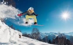 Snowboarder che salta su una pista innevata in montagna con cielo sereno
