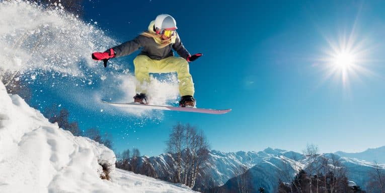 Snowboarder che salta su una pista innevata in montagna con cielo sereno