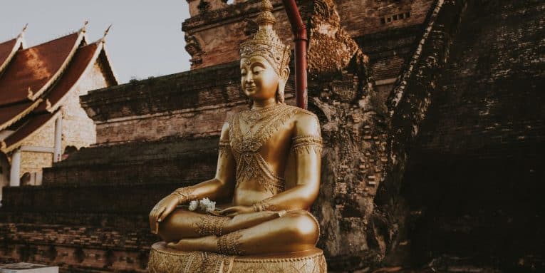 Statua dorata di Buddha seduto davanti a un tempio