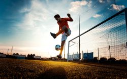 Giocatore di calcio che palleggia con il pallone vicino alla porta al tramonto