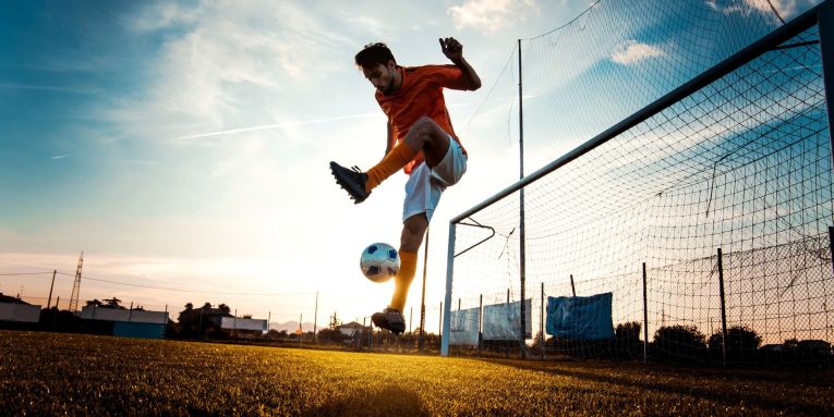 Giocatore di calcio che palleggia con il pallone vicino alla porta al tramonto