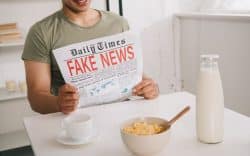 Persona seduta a tavola che legge un giornale con scritta “fake news”