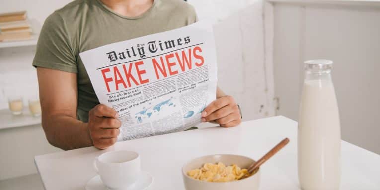 Persona seduta a tavola che legge un giornale con scritta “fake news”