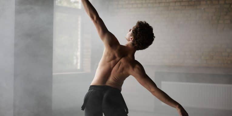 Ballerino di schiena che esegue un passo di danza in una stanza con luce naturale