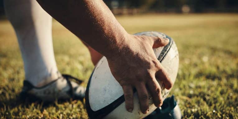 Mano che appoggia un pallone da rugby sull’erba