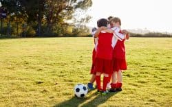 Gruppo di bambini con divisa da calcio riuniti in cerchio su prato con pallone
