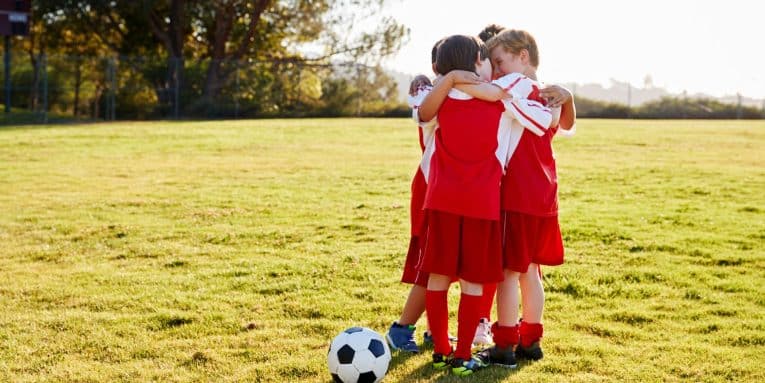 Gruppo di bambini con divisa da calcio riuniti in cerchio su prato con pallone