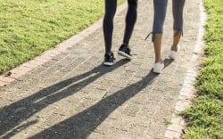 Dettaglio delle gambe di due persone che camminano su un percorso pavimentato con erba ai lati
