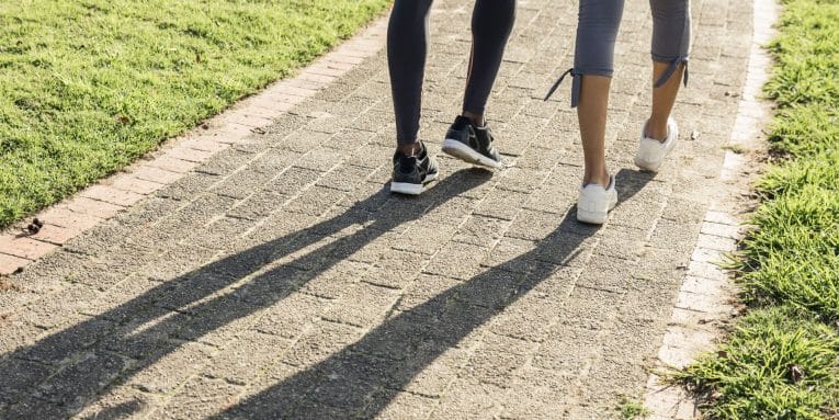 Dettaglio delle gambe di due persone che camminano su un percorso pavimentato con erba ai lati