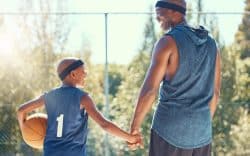 Adulto e bambino che si tengono per mano su un campo da basket con pallone