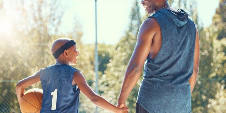 Adulto e bambino che si tengono per mano su un campo da basket con pallone