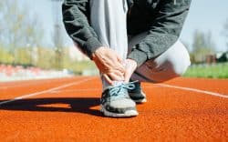 Persona accovacciata su pista da corsa mentre si tiene la caviglia