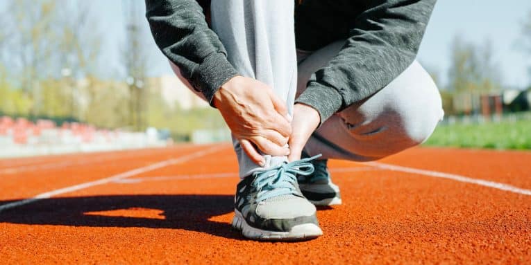 Persona accovacciata su pista da corsa mentre si tiene la caviglia