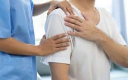 Persona che si tiene la spalla mentre un operatore sanitario appoggia le mani sulla zona