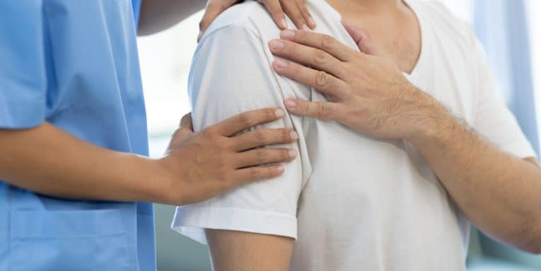 Persona che si tiene la spalla mentre un operatore sanitario appoggia le mani sulla zona