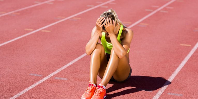 Atleta seduta su pista di atletica con le mani sul volto