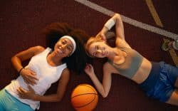 due persone sorridenti sdraiate a terra accanto a un pallone da basket