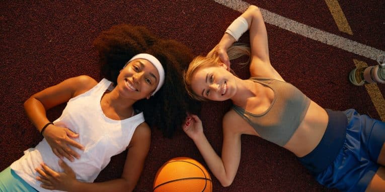 due persone sorridenti sdraiate a terra accanto a un pallone da basket