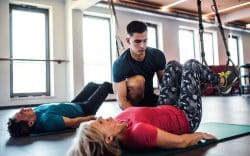 persona sdraiata su tappetino con gambe piegate e sollevate assistita da personal trainer