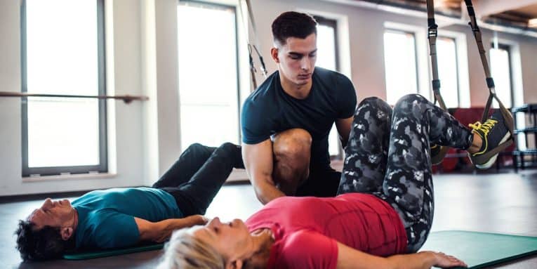 persona sdraiata su tappetino con gambe piegate e sollevate assistita da personal trainer