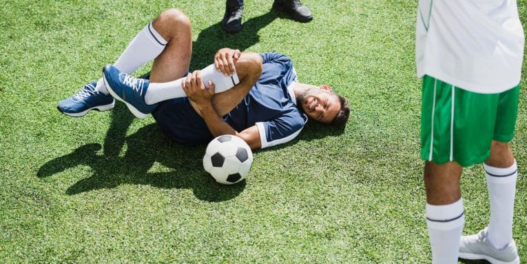 persona sdraiata su erba con una gamba piegata mentre si tiene il ginocchio