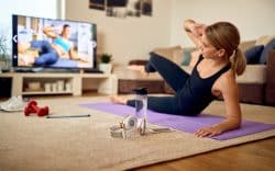 persona sdraiata su tappetino in casa con abbigliamento sportivo mentre segue un allenamento su uno schermo