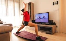 persona in casa con abbigliamento sportivo mentre si allena su tappetino seguendo esercizi su uno schermo