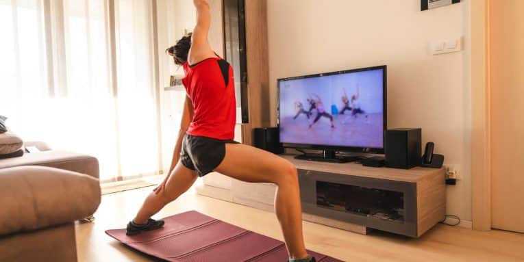 persona in casa con abbigliamento sportivo mentre si allena su tappetino seguendo esercizi su uno schermo