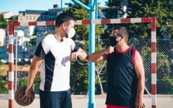 due persone con abbigliamento sportivo che indossano la mascherina mentre si salutano con il gomito su un campo da basket