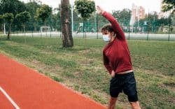 persona con abbigliamento sportivo mentre fa stretching su una pista all’aperto con mascherina