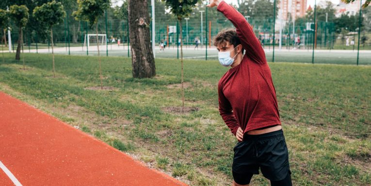 persona con abbigliamento sportivo mentre fa stretching su una pista all’aperto con mascherina