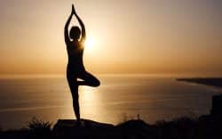persona che pratica yoga al tramonto su una scogliera vista mare