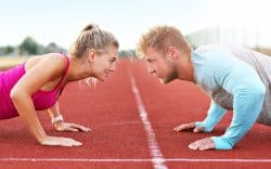 uomo e donna uno di fronte all’altro fanno flessioni su pista di atletica