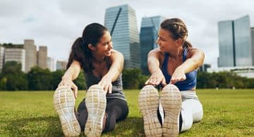 due donne fanno stretching all’aperto sedute sull’erba