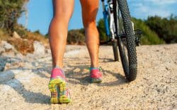 dettaglio polpacci di persona che cammina accanto a una bicicletta su un sentiero sterrato.