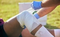 Persona che fascia il ginocchio di un atleta in campo.