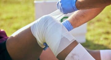 Persona che fascia il ginocchio di un atleta in campo.